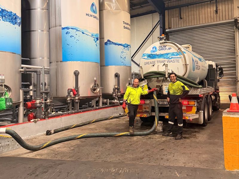 Two HLW Group workers beside a grease trap waste truck at a treatment facility